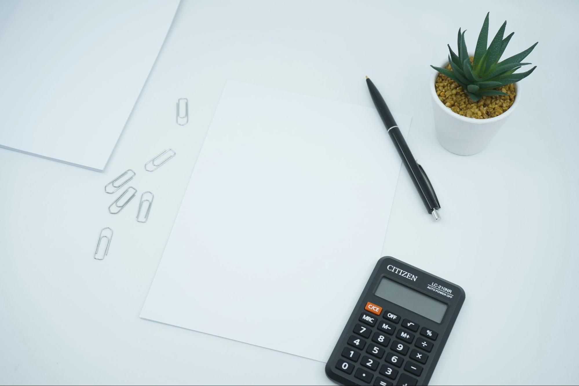 A pen, calculator, paper clips, and paper on a desk for calculating attrition