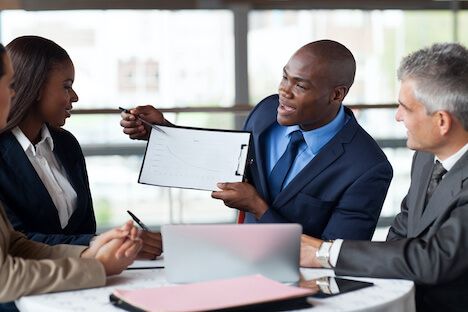 Man showing a clipboard with a sales chart to a group of people