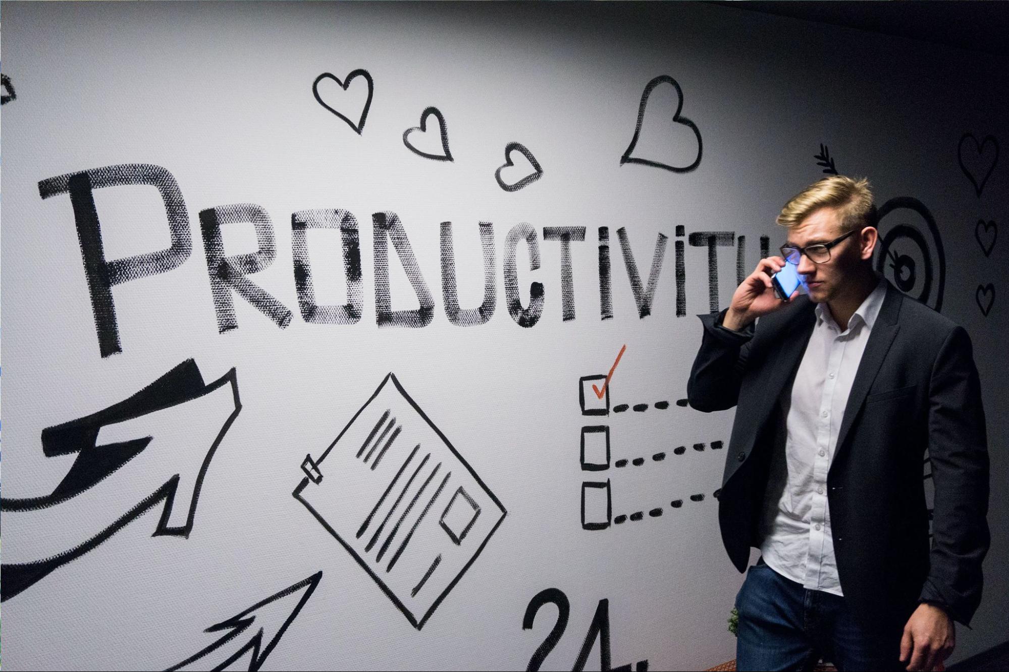 Sales professional with phone walking by productivity wall